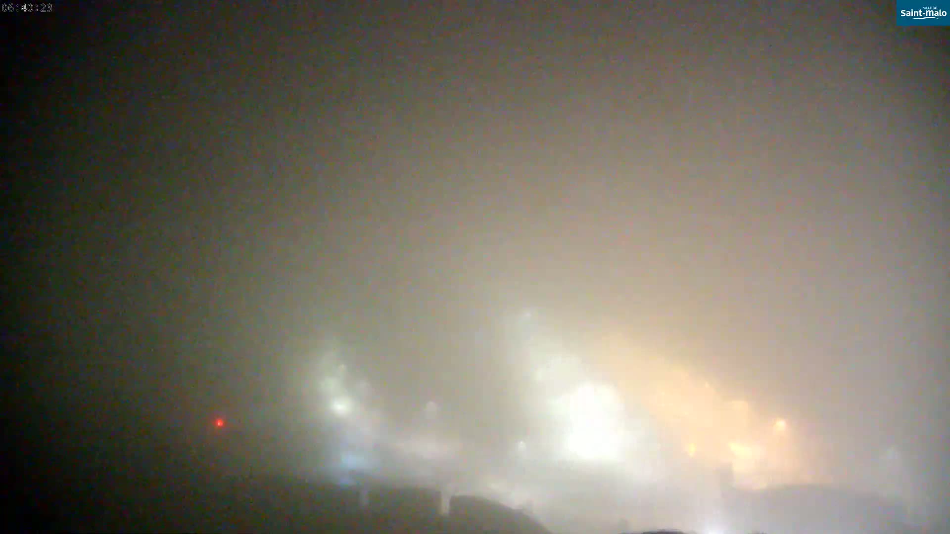 Faintly lit structures are barely visible through a thick fog.