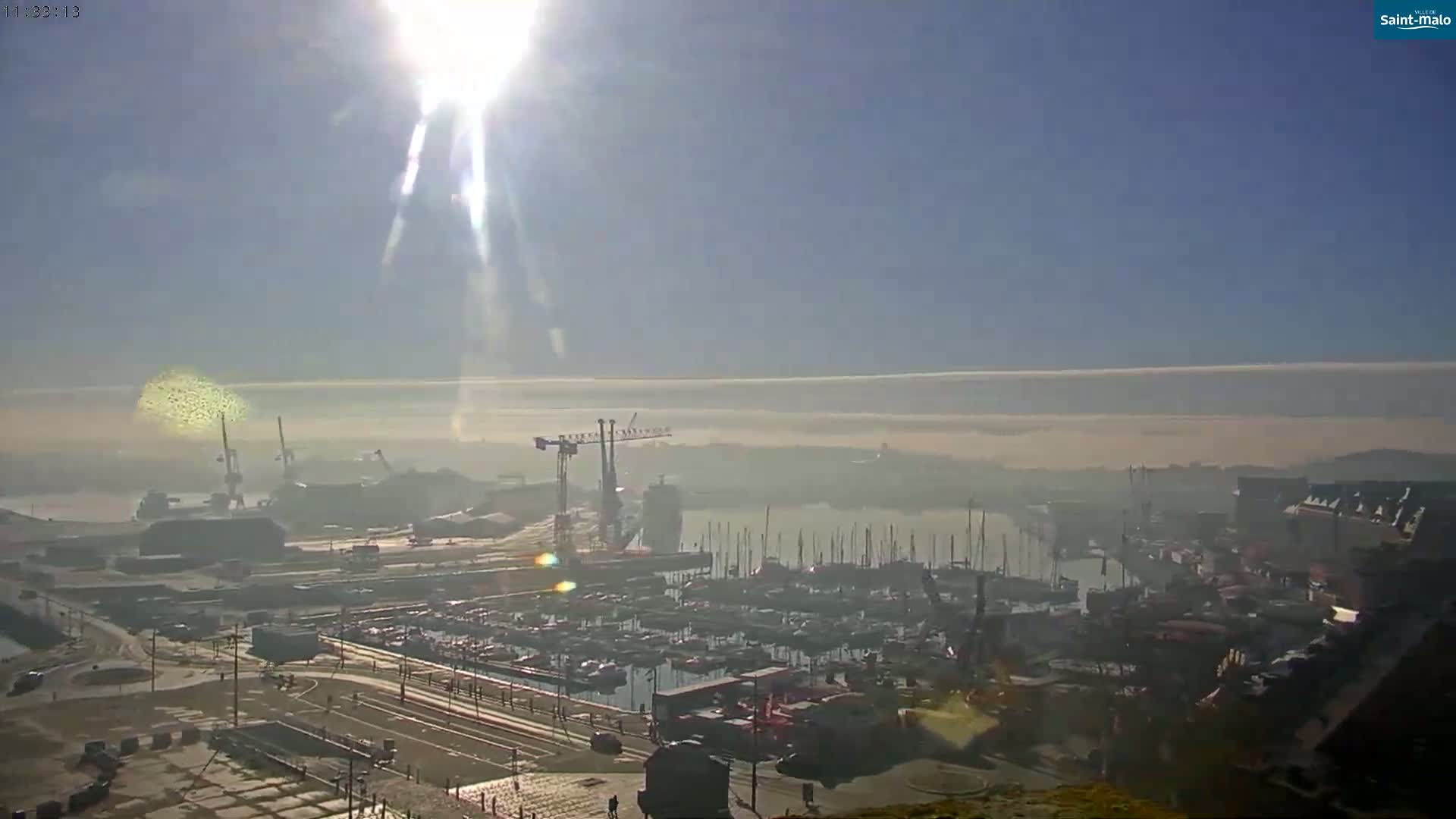 A sunny day with hazy fog over a harbor filled with boats and industrial areas with cranes.