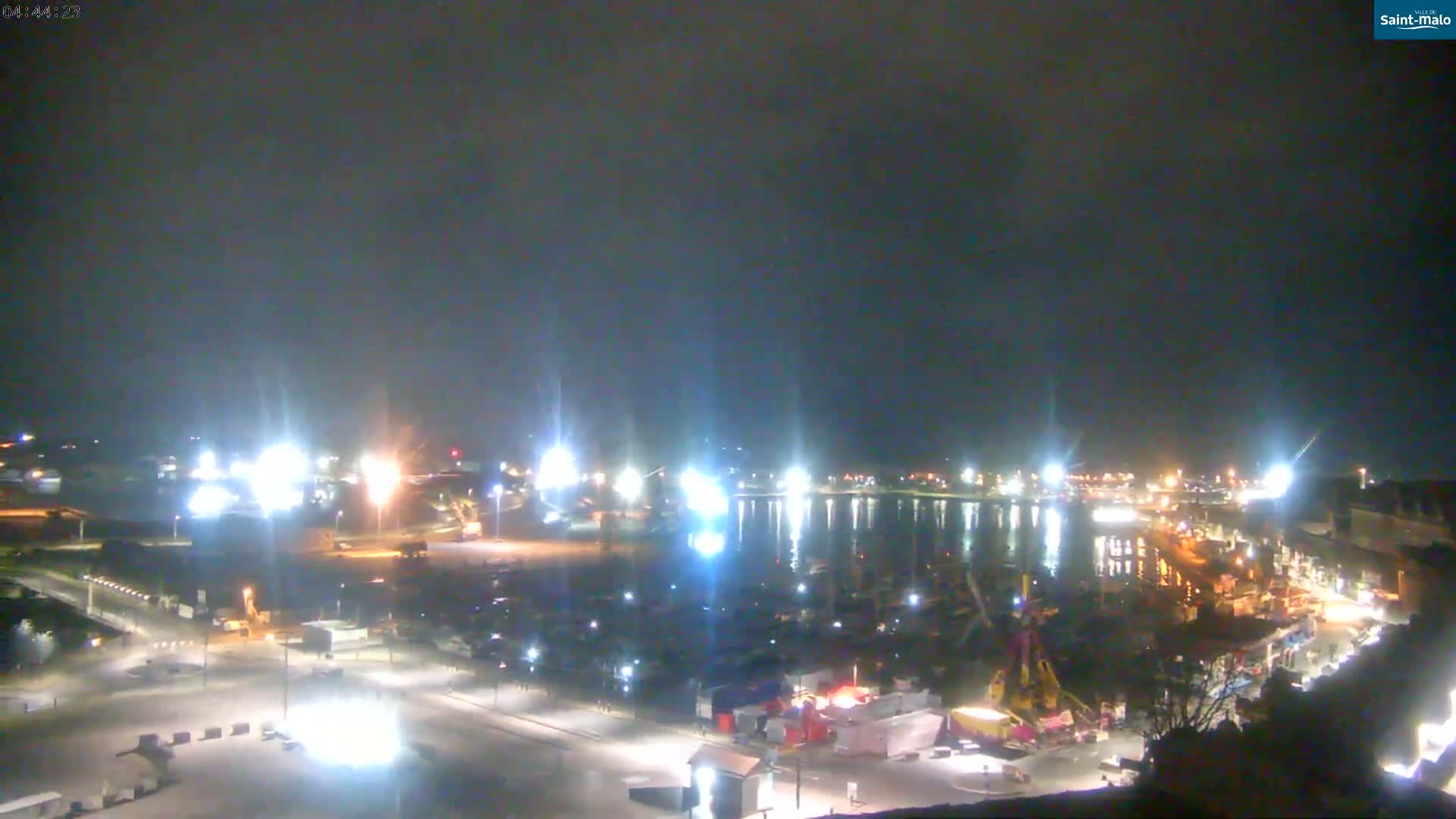 A nighttime, high-angle view of a harbor filled with boats and surrounded by brightly lit buildings and roads.