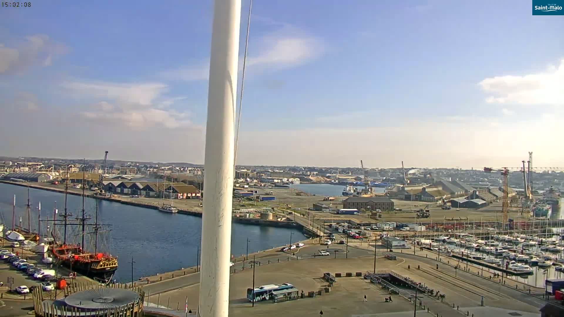 A mostly sunny day overlooks a harbor filled with sailboats and ships, with a city in the distance.