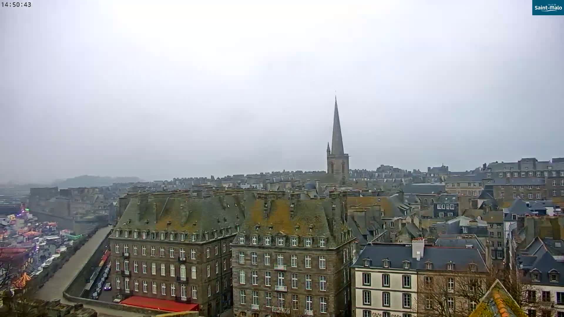 A hazy view overlooking a European city with many grey-roofed buildings and a tall church spire, on an overcast day.