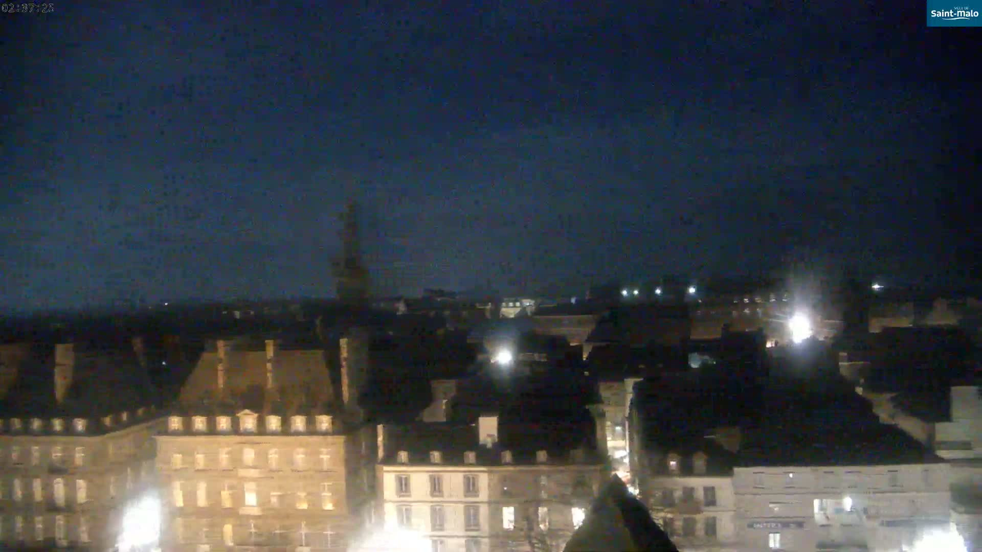 A nighttime, long shot of a city with many buildings lit up under a dark, clear sky.
