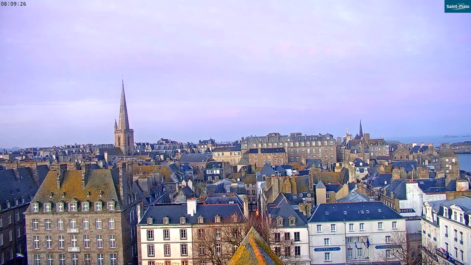 A panoramic view of a city with many closely-packed buildings under a pale purple sky.
