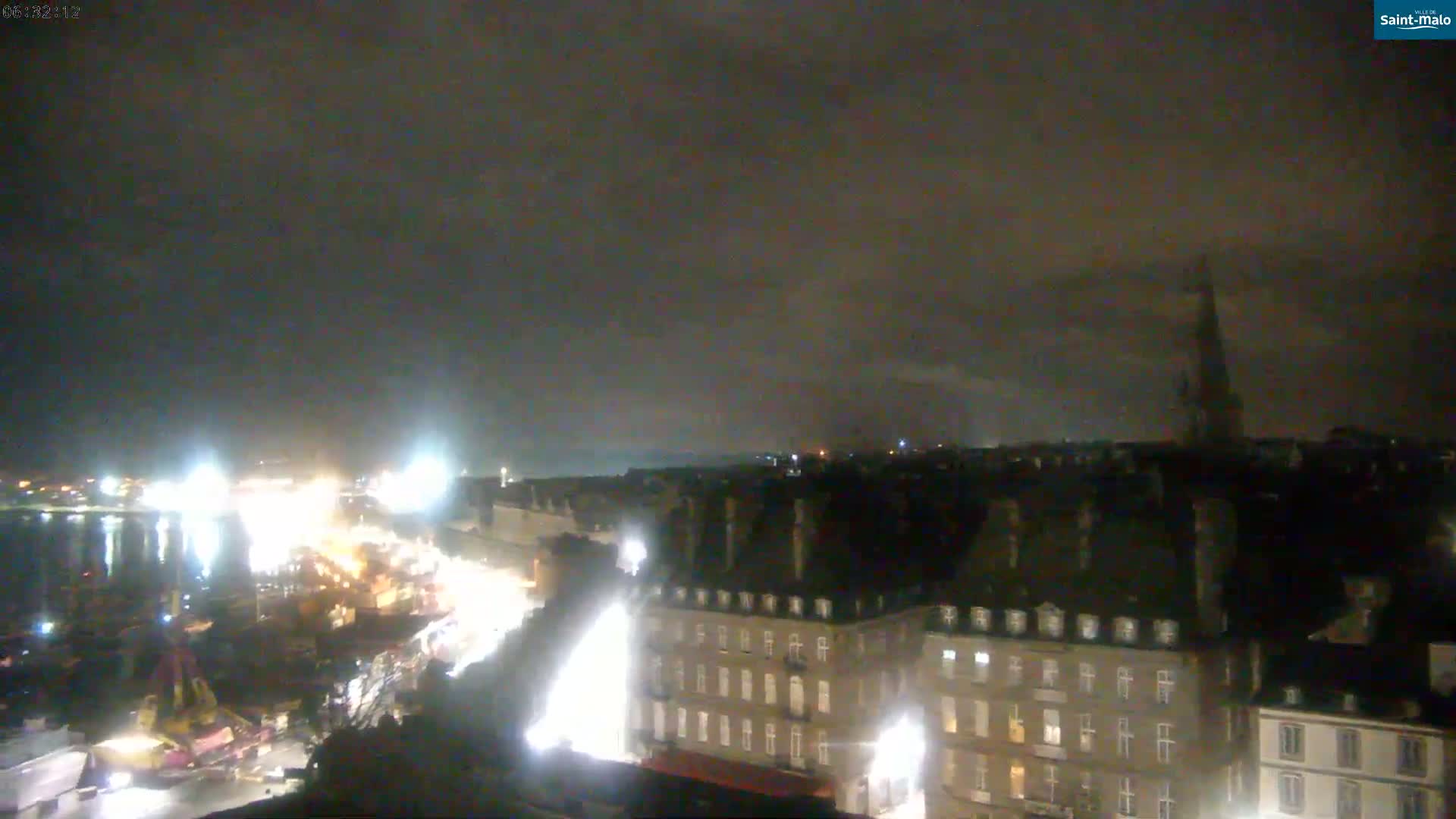 A nighttime view of a city harbor and buildings under a cloudy sky.