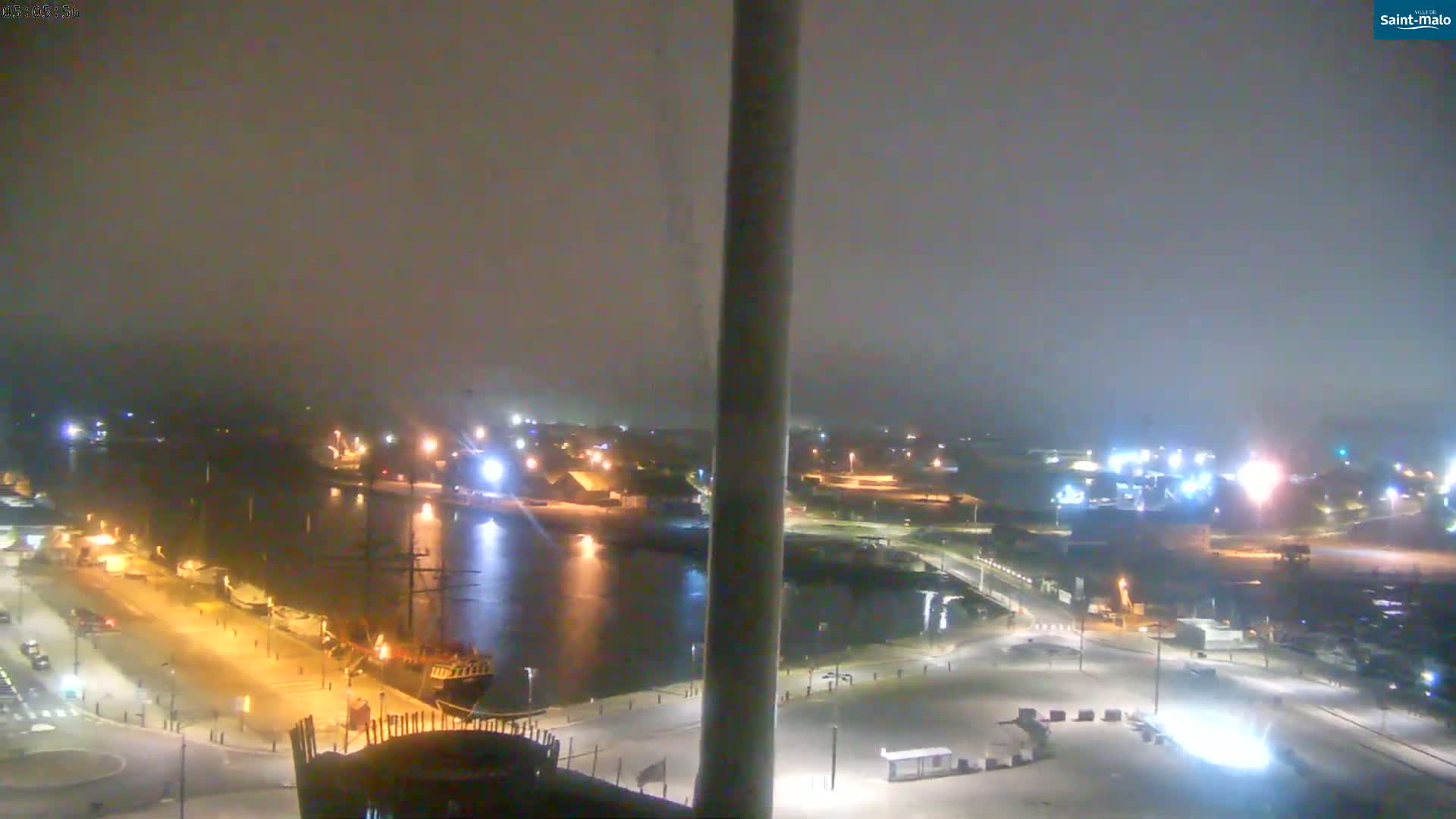 A nighttime, hazy view of a harbor with docked ships and illuminated buildings along a waterfront.