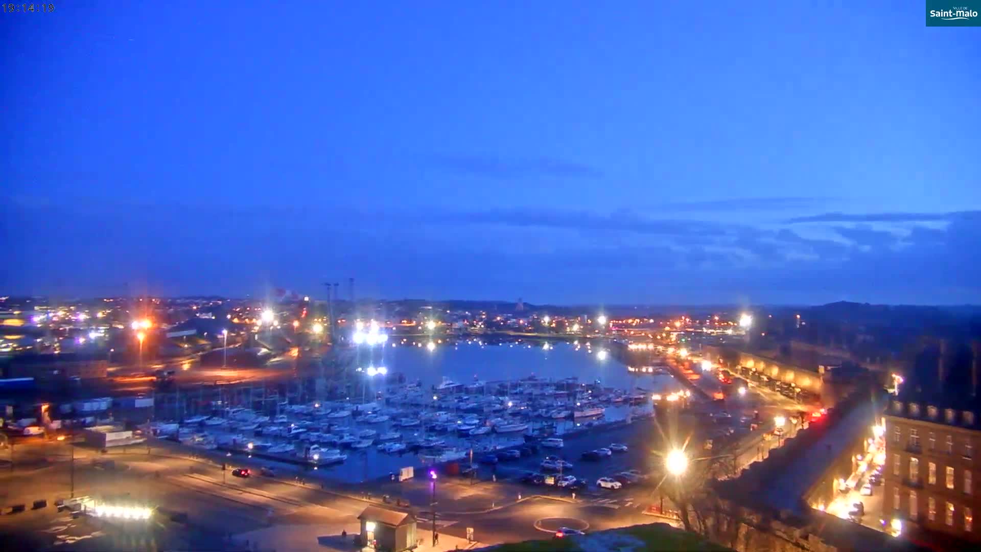 A harbor filled with boats is illuminated at twilight under a clear, dark-blue sky.