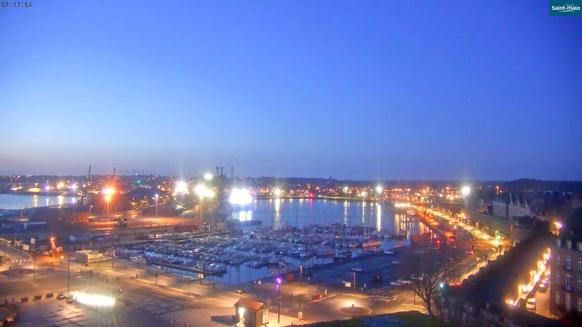 A harbor filled with boats is illuminated at twilight under a clear, dark-blue sky.