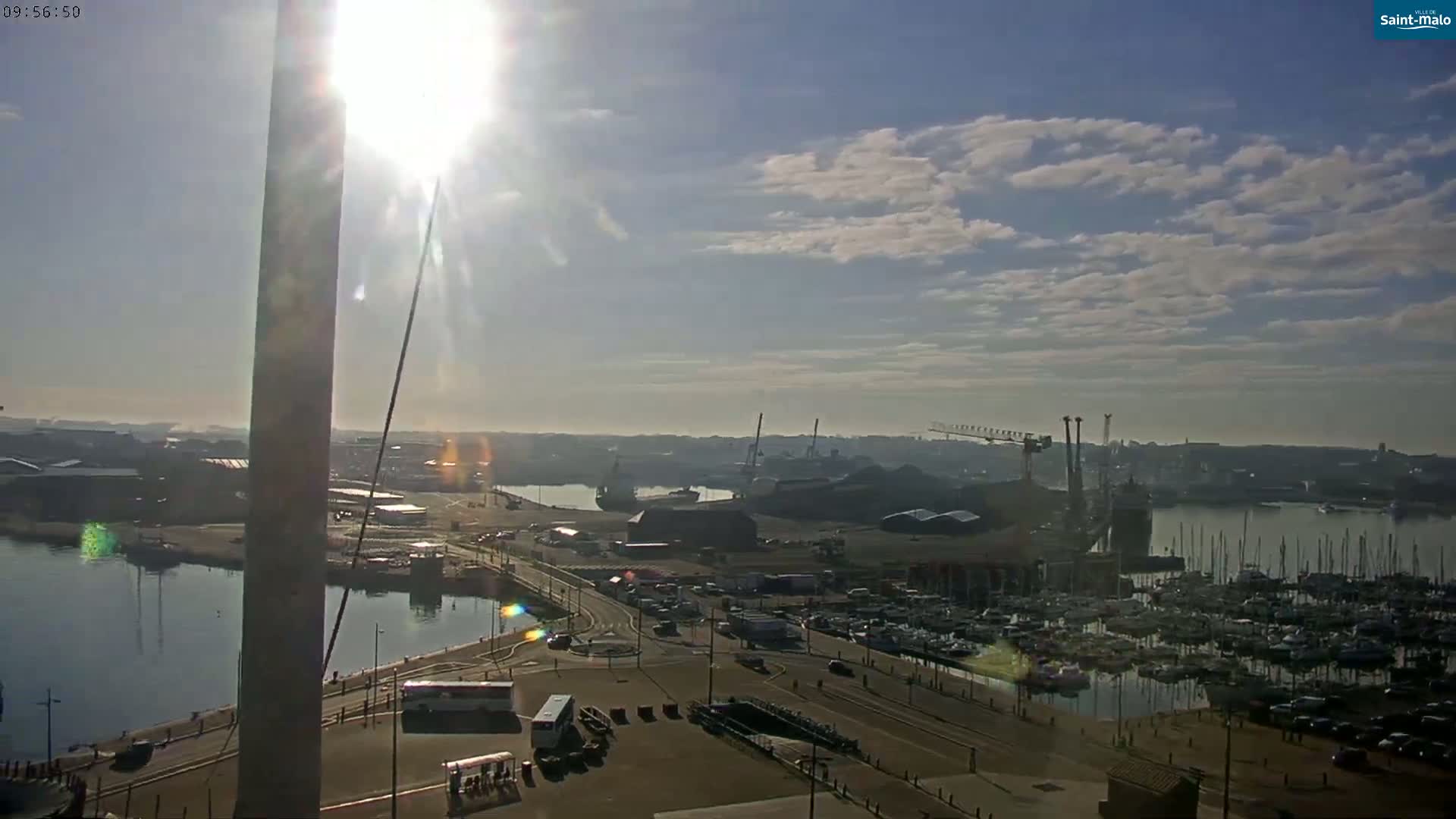 A sunny day reveals a harbor filled with numerous boats and ships, alongside industrial areas and roads.