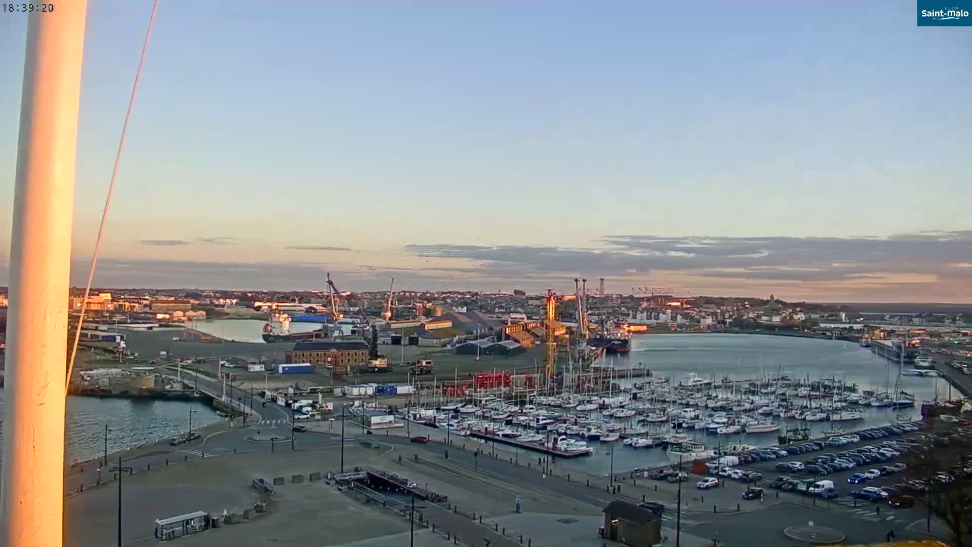 A harbor filled with numerous sailboats and other vessels at sunset under a mostly clear sky.