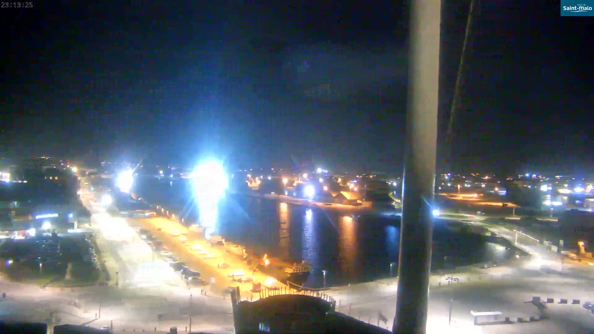 A nighttime, high-angle view of a harbor illuminated by artificial lights, with a calm body of water reflecting the lights.