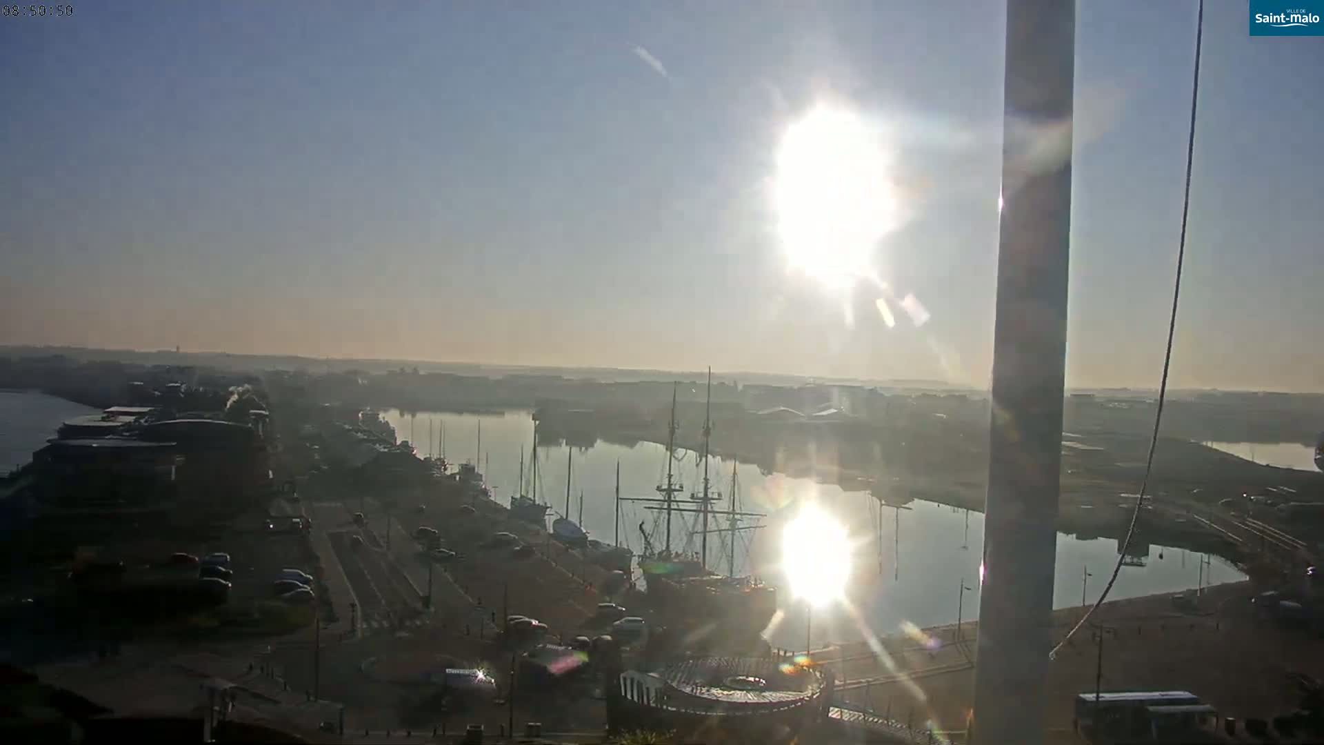 A hazy sunrise illuminates a harbor filled with boats and ships, viewed from an elevated vantage point.