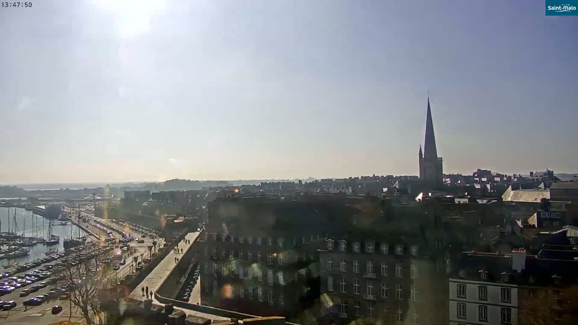 A sunny day overlooking a harbor filled with boats and a city with a tall church spire.