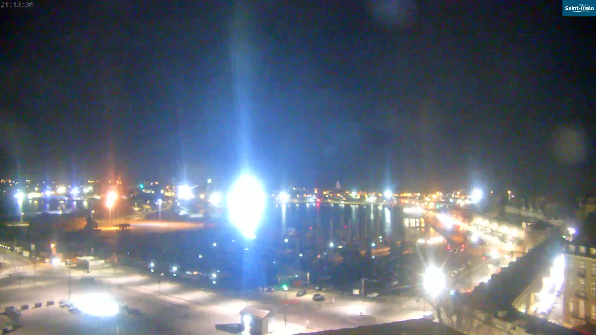 A nighttime, high-angle view of a harbor town with its lights reflecting on the water under a clear, dark sky.