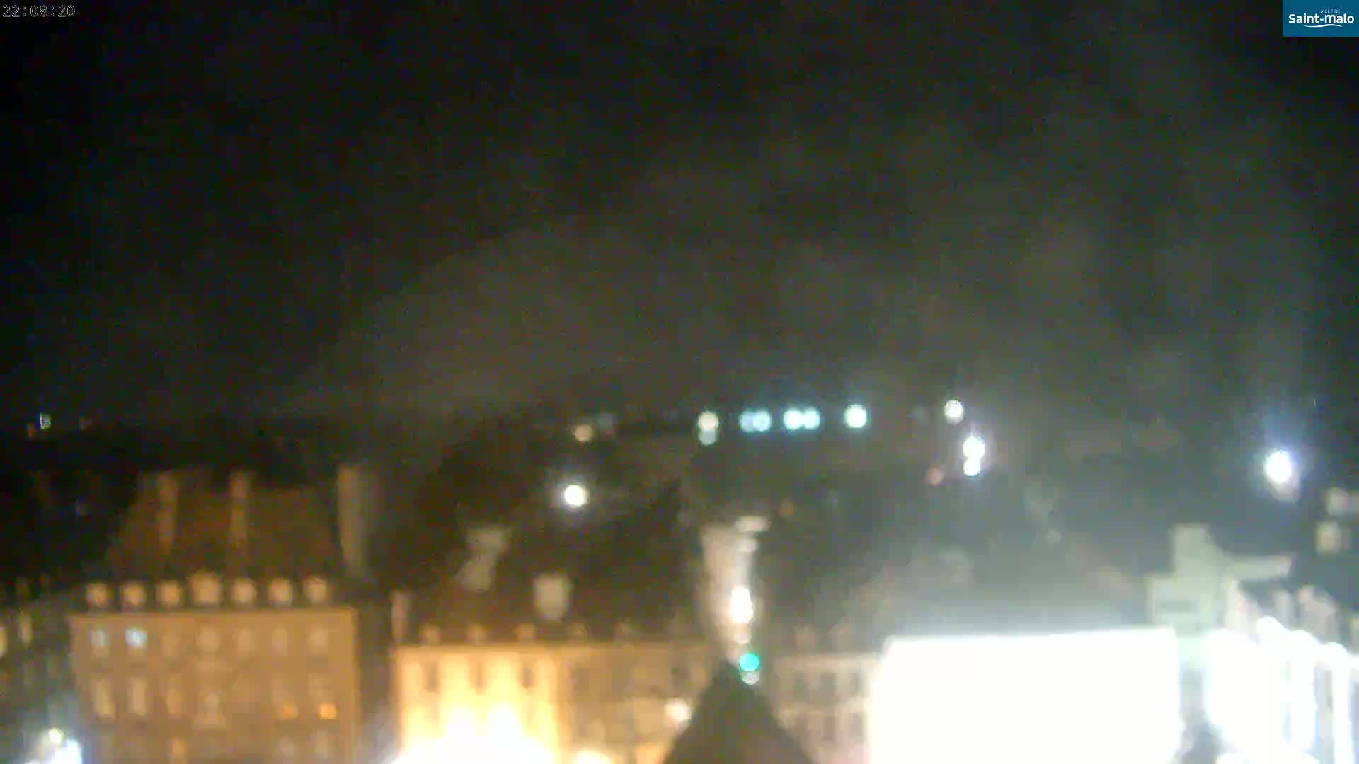 A nighttime, blurry view of a city with dimly lit buildings under a dark, cloudy sky.