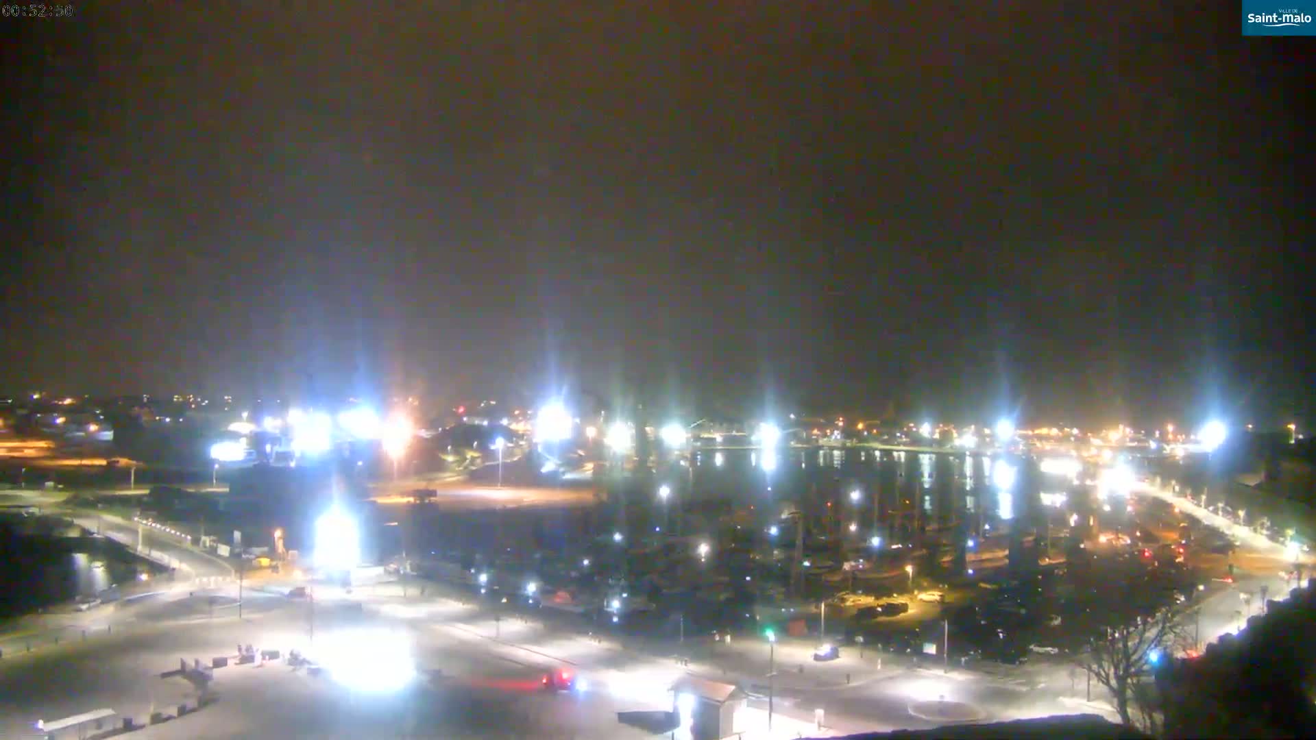 A nighttime, snowy view of a harbor filled with boats, surrounded by brightly lit streets and buildings.
