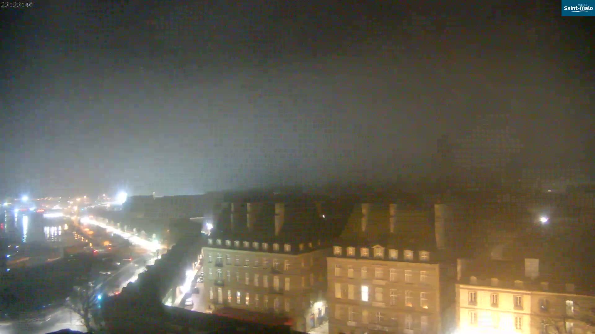 A nighttime, foggy view of a city showing a long street with cars and buildings lit up.