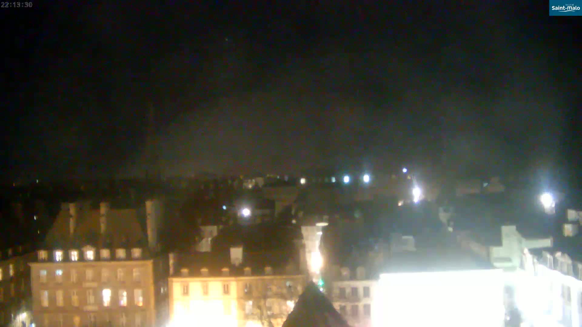 A nighttime view of a city with many buildings lit up under a dark, cloudy sky.