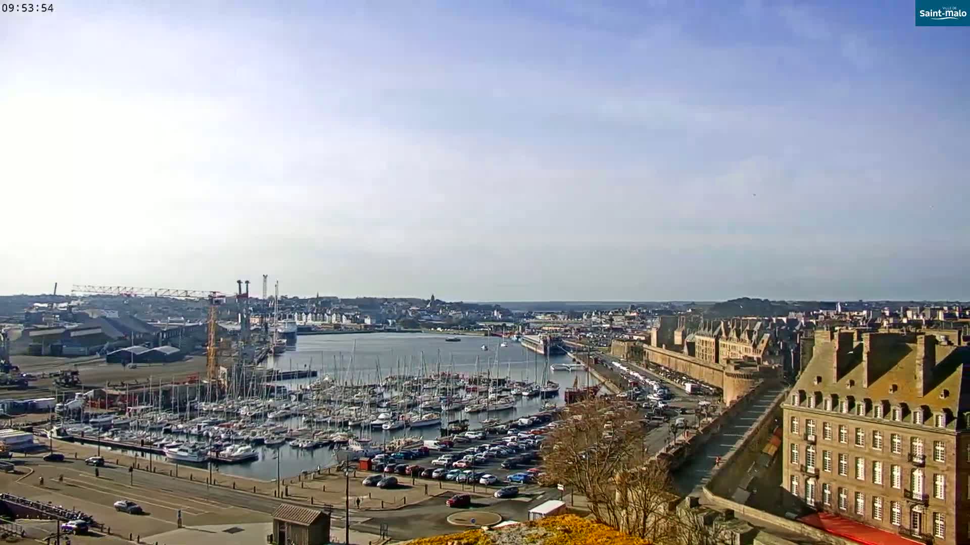 A harbor filled with numerous sailboats and yachts is situated beneath a mostly clear sky next to a city with historic-looking buildings.