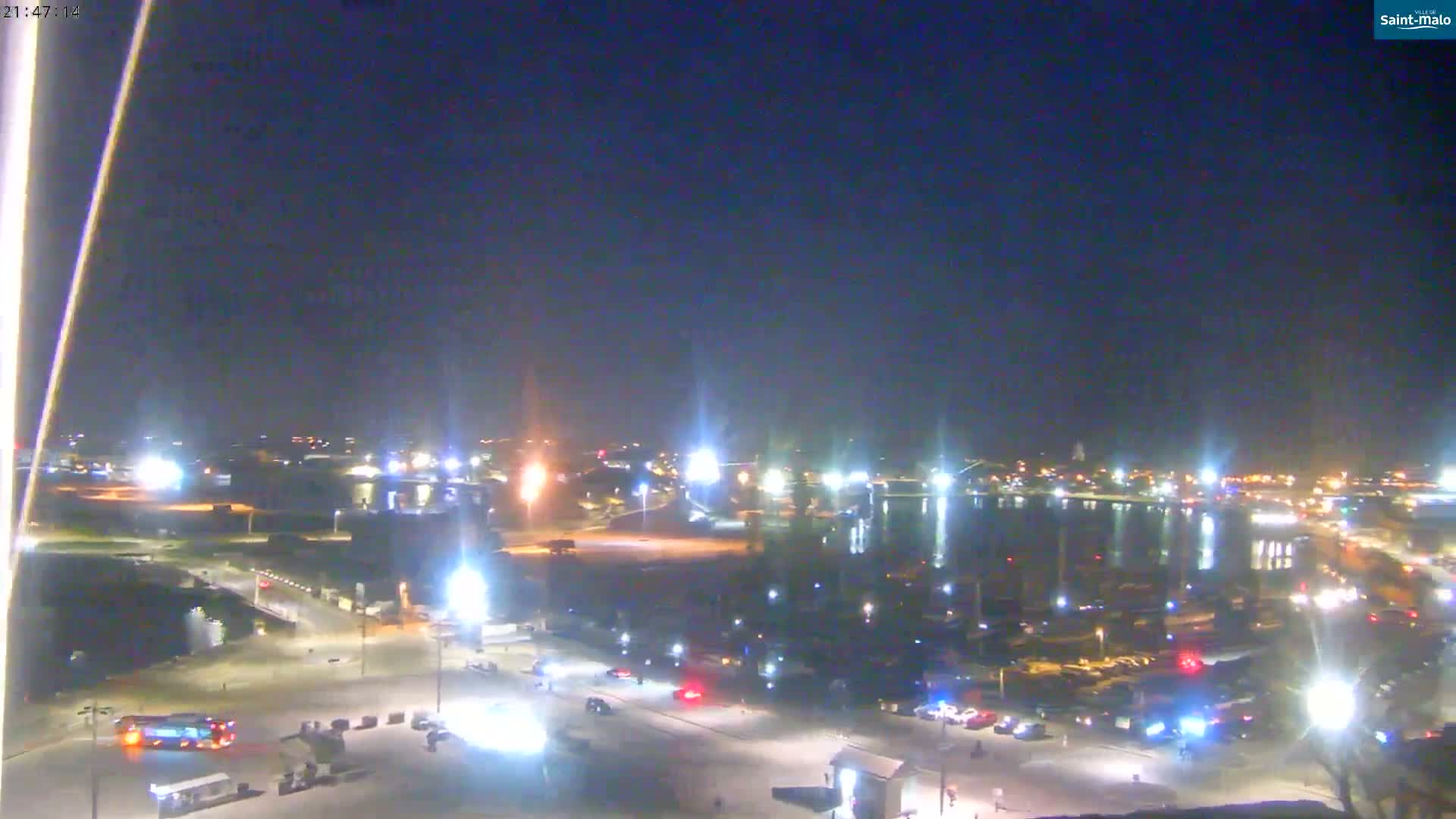 A nighttime view of a waterfront area with scattered vehicles and lights, under a clear, dark sky.