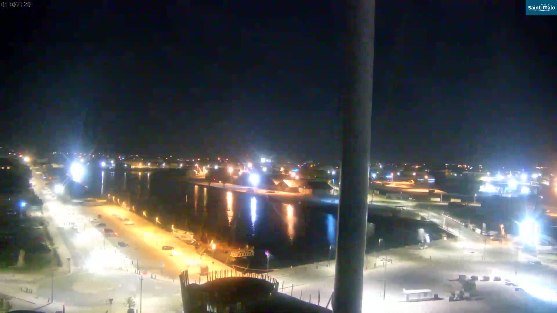 A nighttime view of a harbor and city, illuminated by streetlights and building lights, under a clear, dark sky.