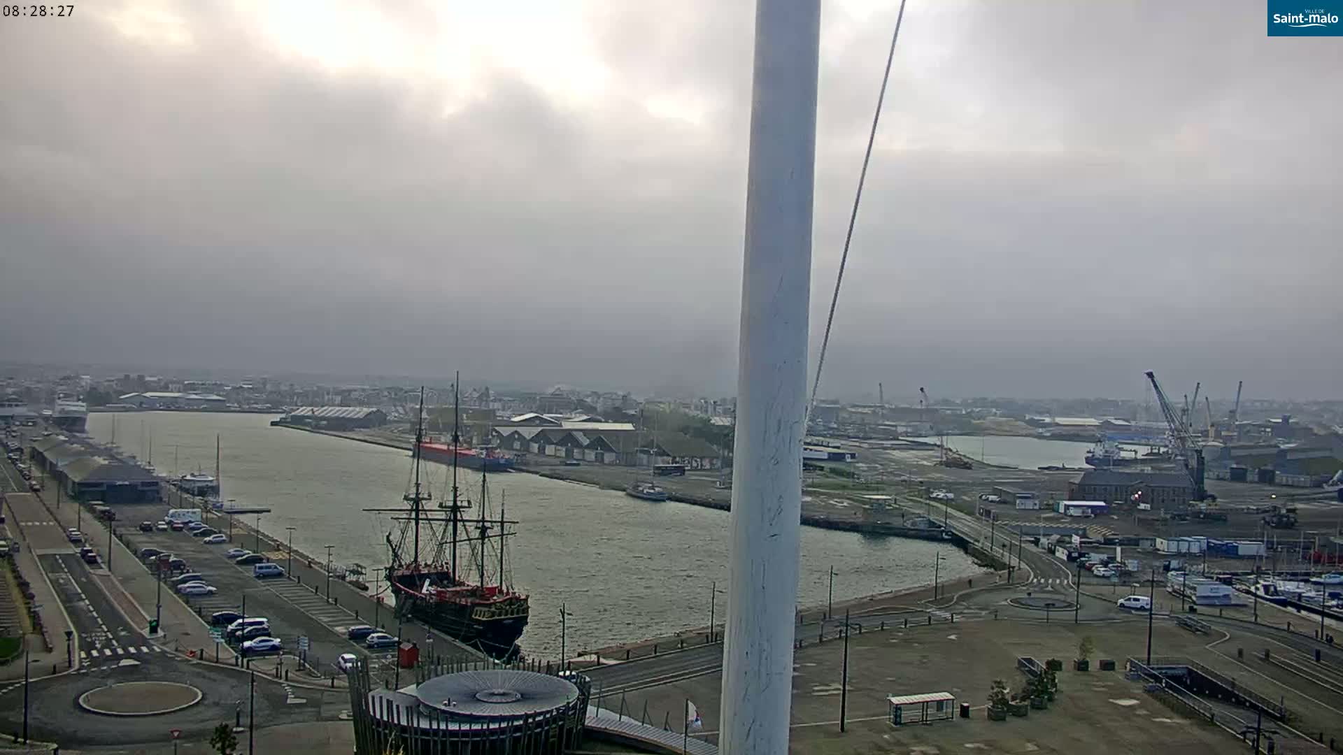 A large sailing ship is docked in a harbor under an overcast sky.