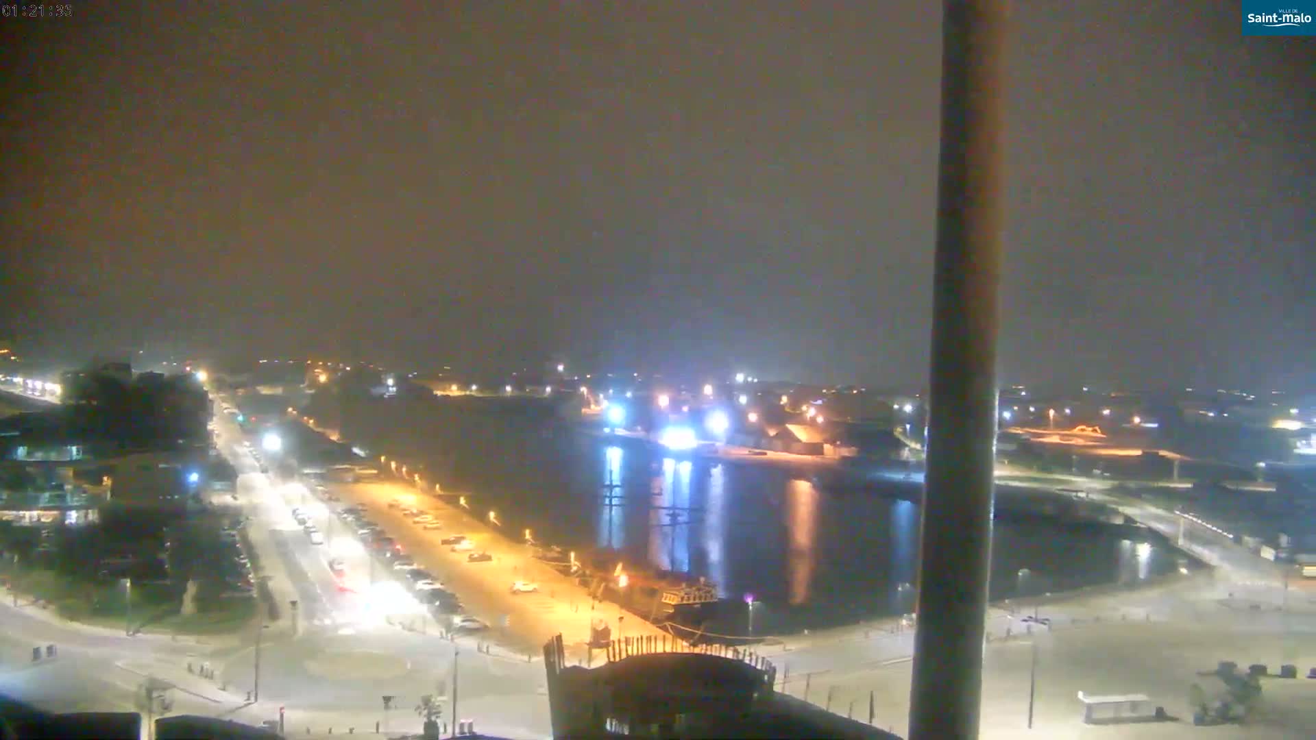 A nighttime, hazy view of a harbor with a road and parked cars leading to it.