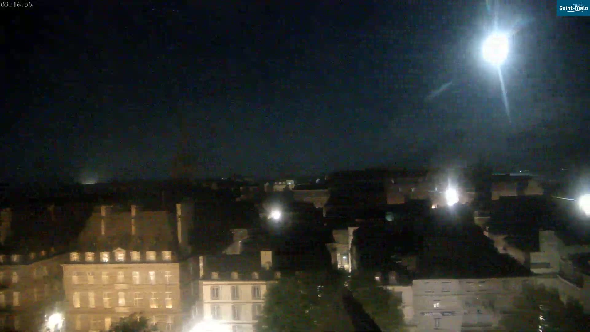 A brightly lit moon shines over a dark city at night.