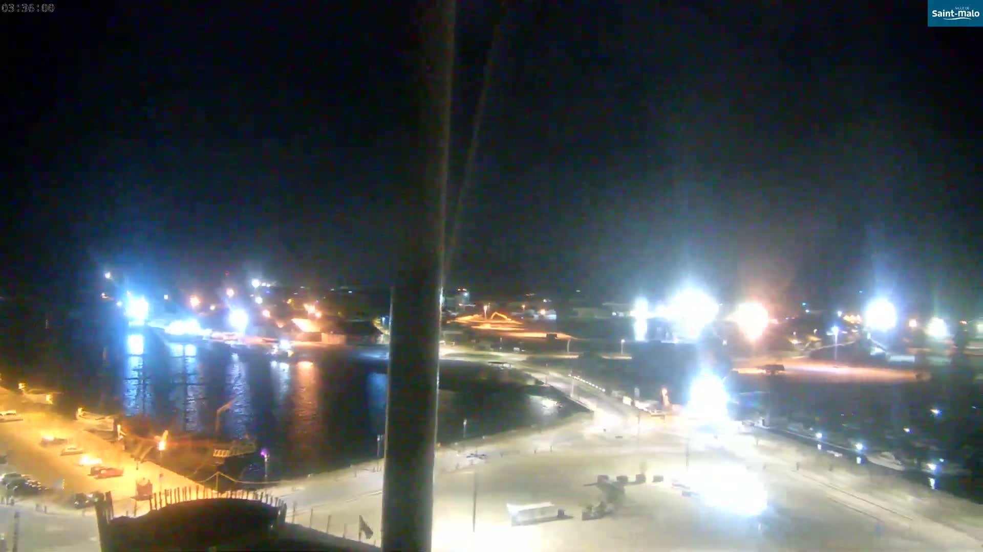 A nighttime view of a harbor with brightly lit boats and docks, under a clear, dark sky.
