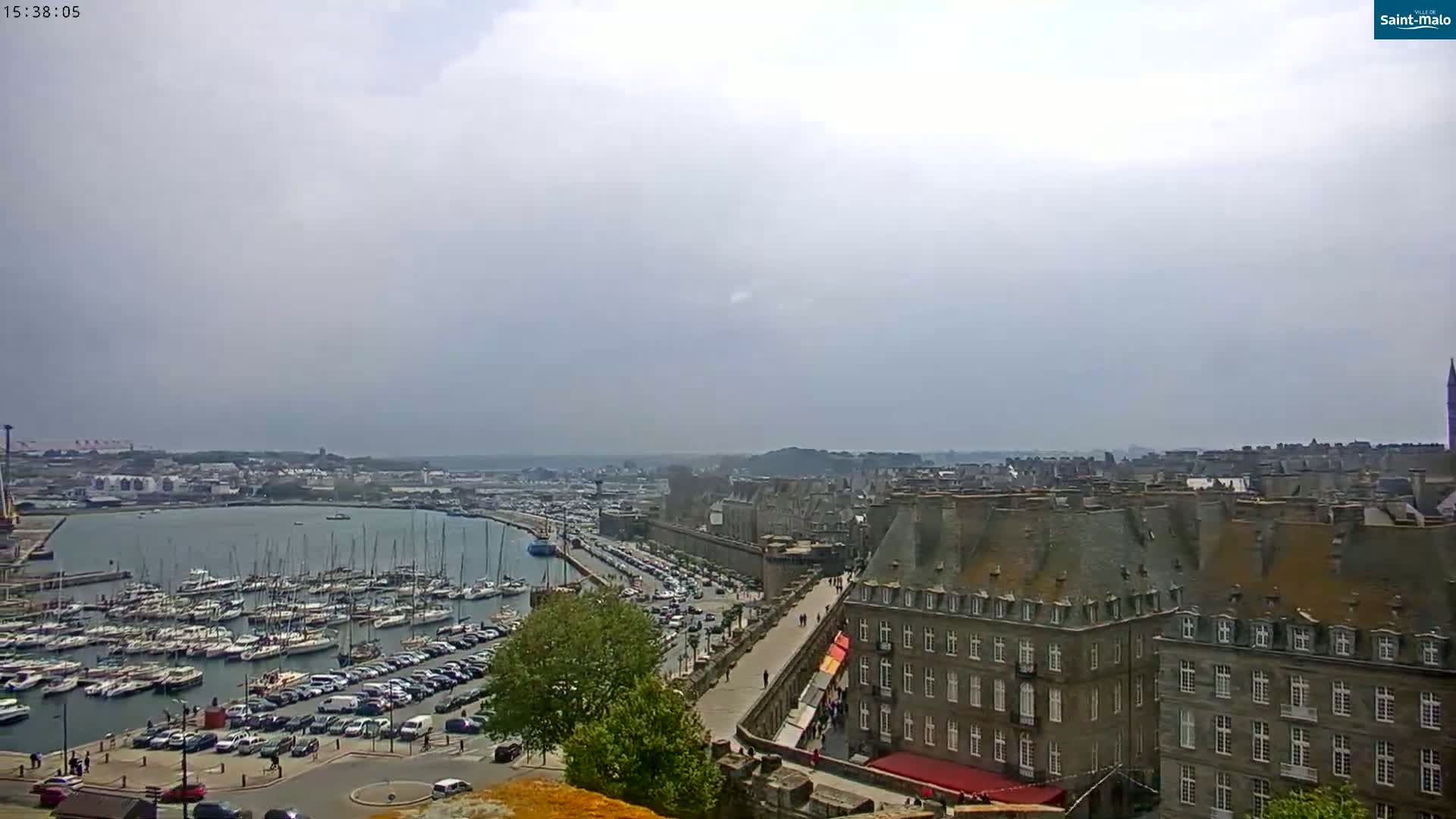 A harbor filled with sailboats is visible below a city of stone buildings under an overcast sky.