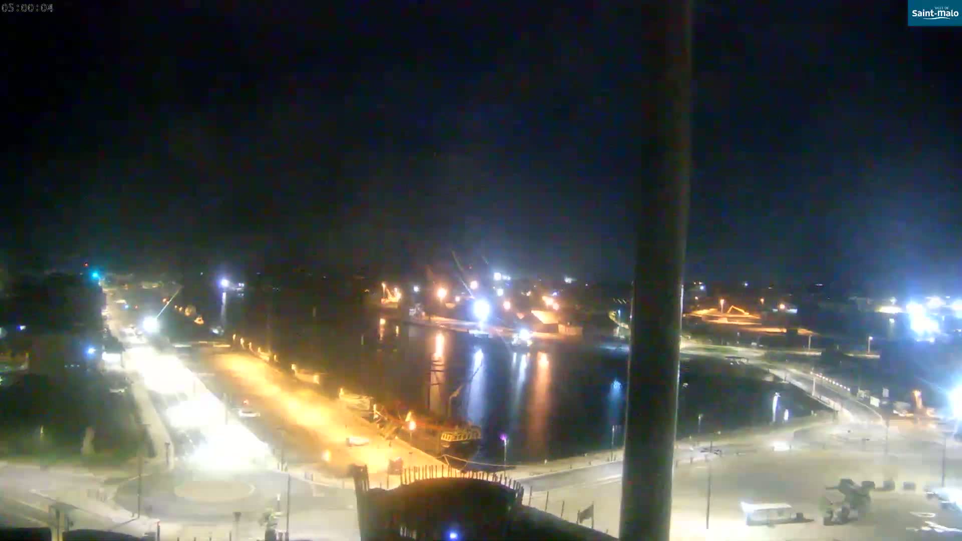 A nighttime, high-angle view shows a harbor with boats and a roadway with traffic.