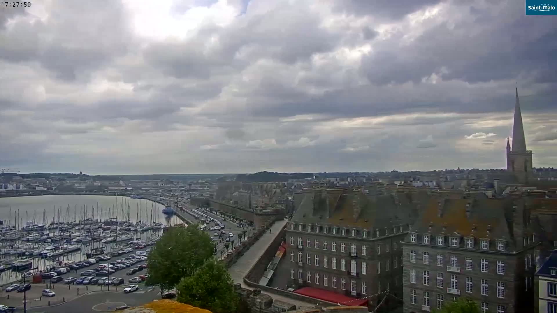 A sprawling coastal town with a marina full of boats is visible under a cloudy sky.
