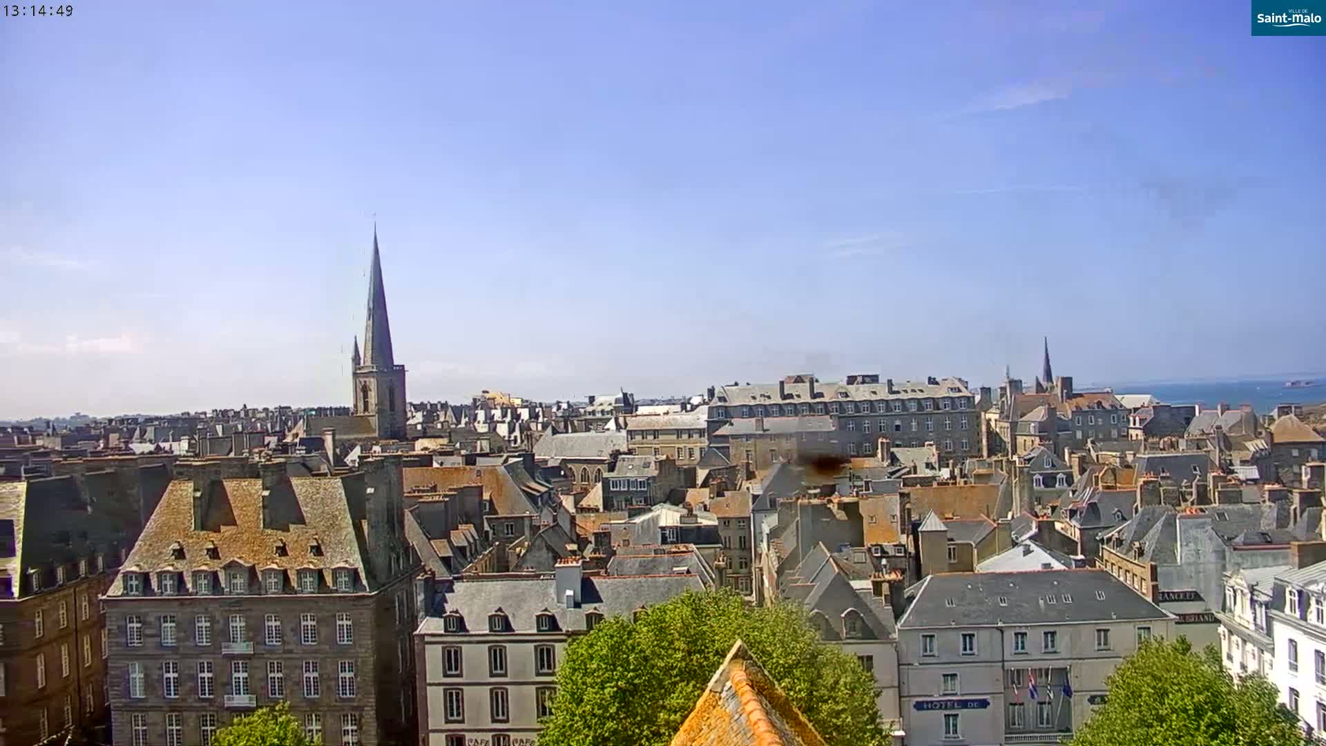 A sprawling cityscape of many closely packed buildings with gray slate roofs under a clear blue sky.