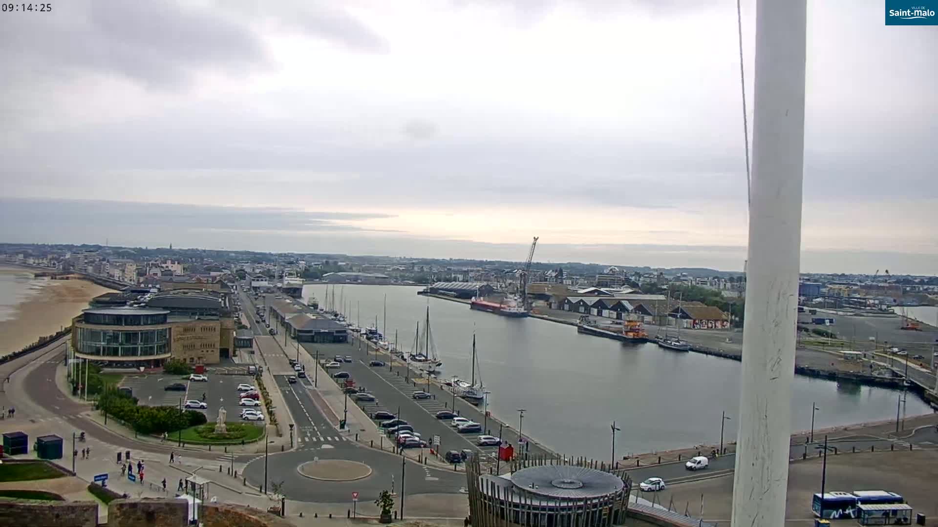 An overcast day reveals a harbor scene with numerous boats, docked ships, and a cityscape beyond, all viewed from a high vantage point.