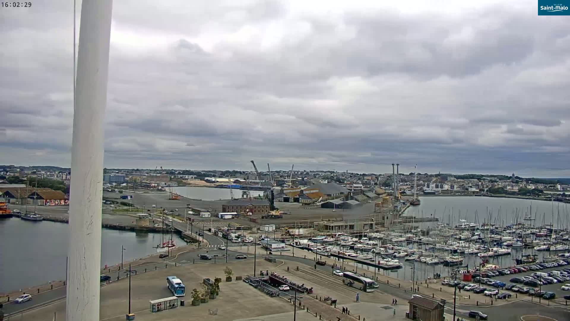 A harbor with numerous boats and a city in the background under a cloudy sky.