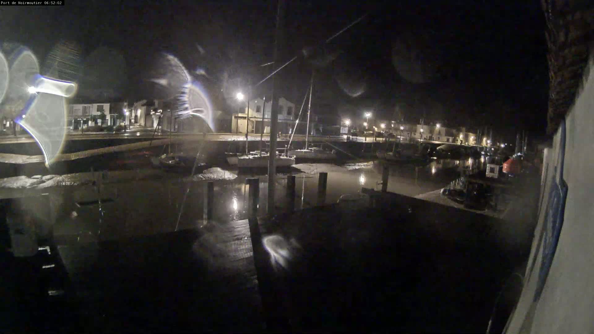 At night, a harbor filled with boats is seen from a dock, under a dark, possibly rainy sky.