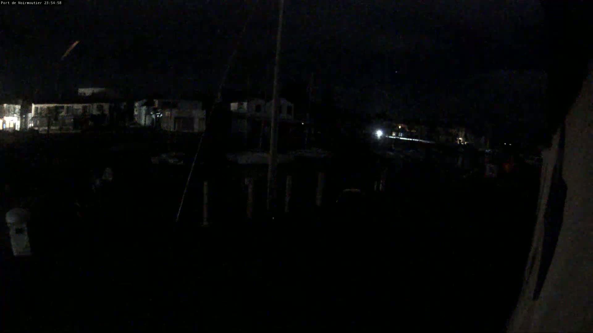 A dark, nighttime scene shows dimly lit buildings in the distance and a mostly dark foreground, possibly a marina.