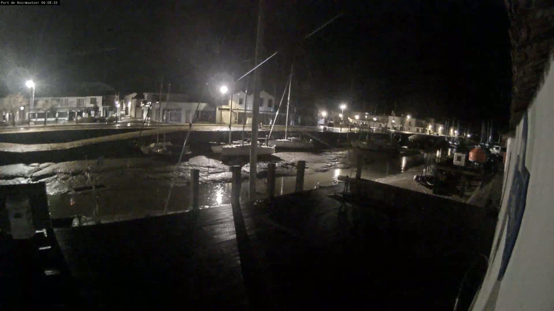 A nighttime view of a harbor with boats resting on exposed mudflats, illuminated by streetlights under a dark sky.