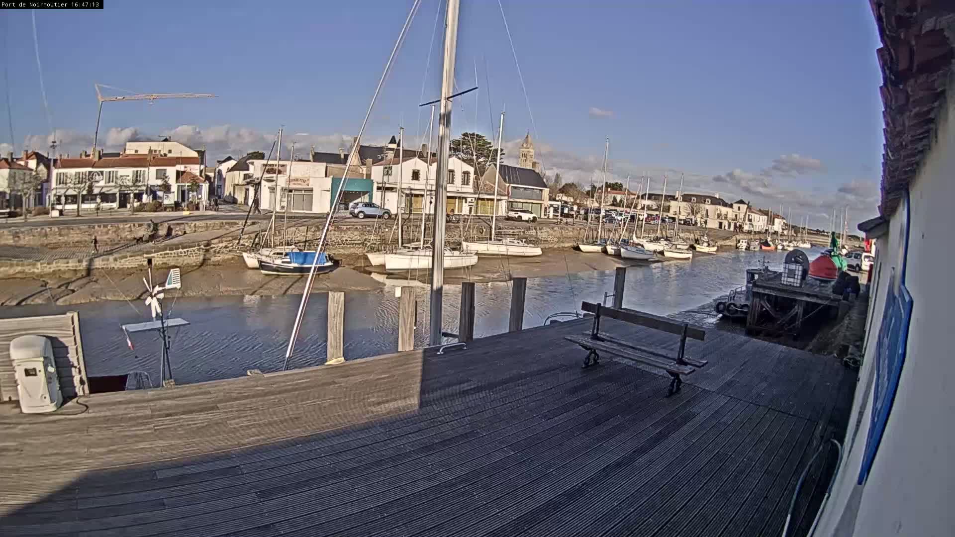 A mostly sunny day reveals a harbor filled with sailboats at low tide, with a town and buildings visible in the background.