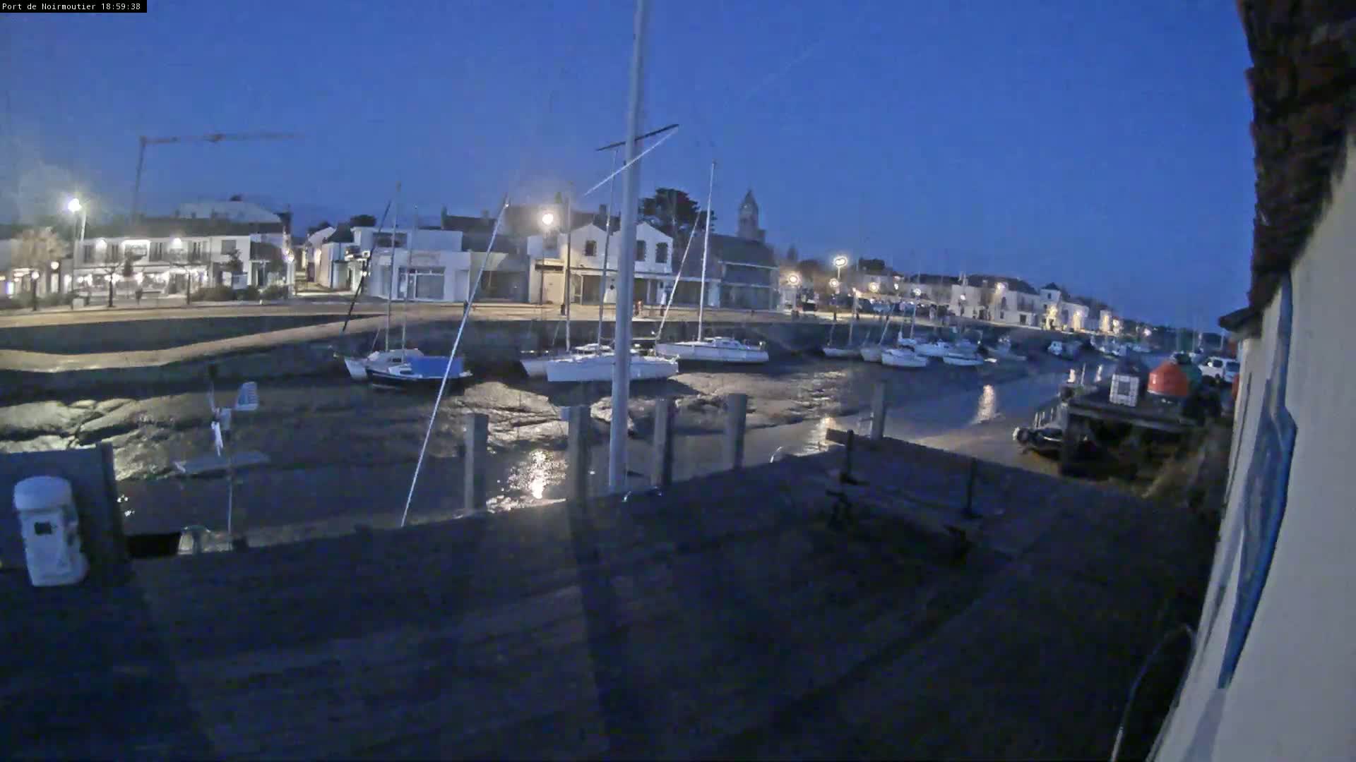 Several sailboats are moored in a harbor at low tide under a twilight sky.