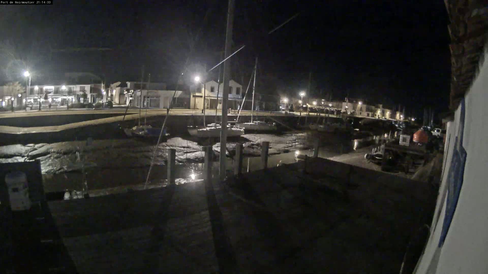 A nighttime view of a harbor with boats docked at low tide, illuminated by streetlights.