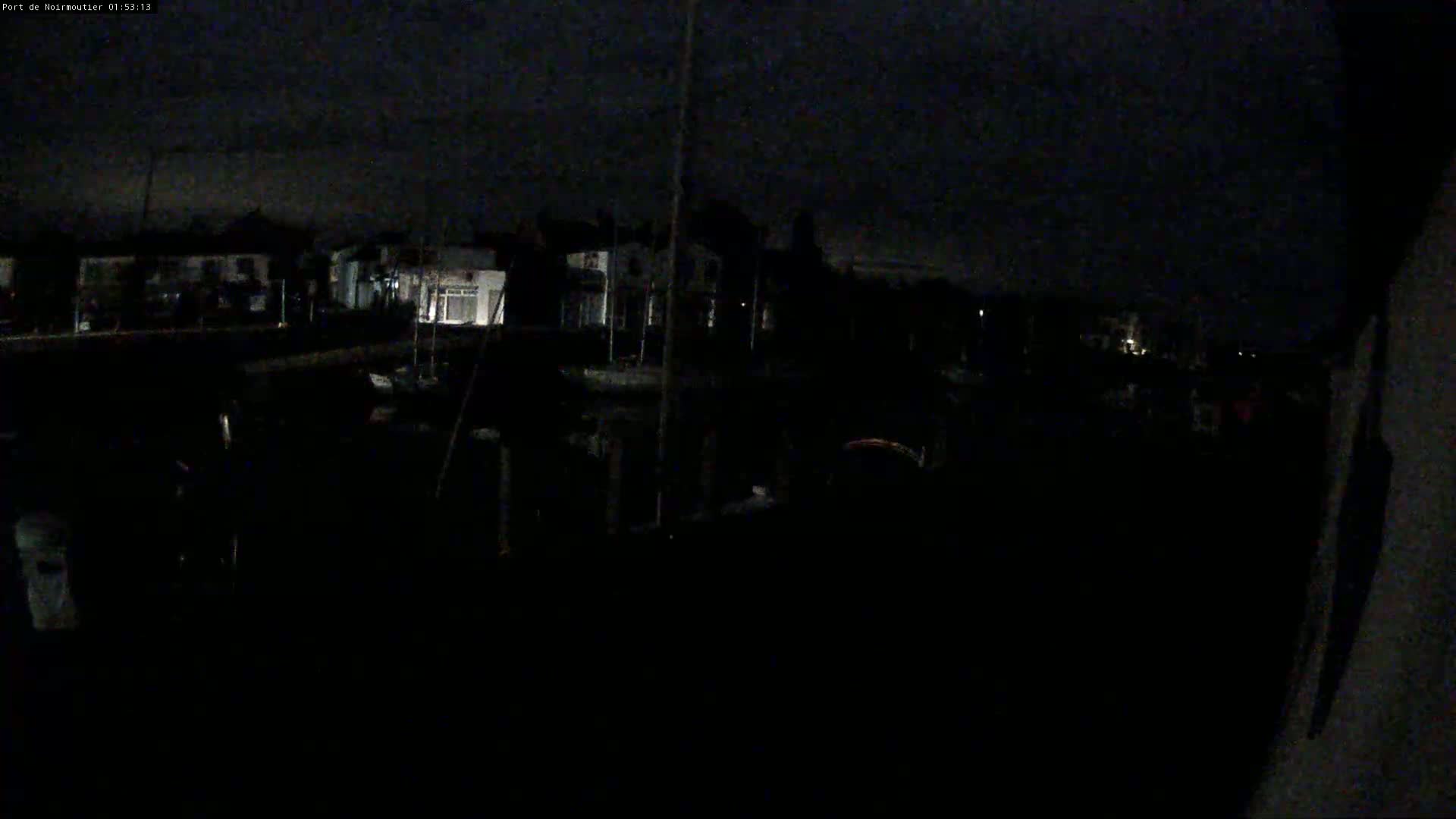 A nighttime view of a dark marina with dimly lit buildings in the background under a cloudy sky.