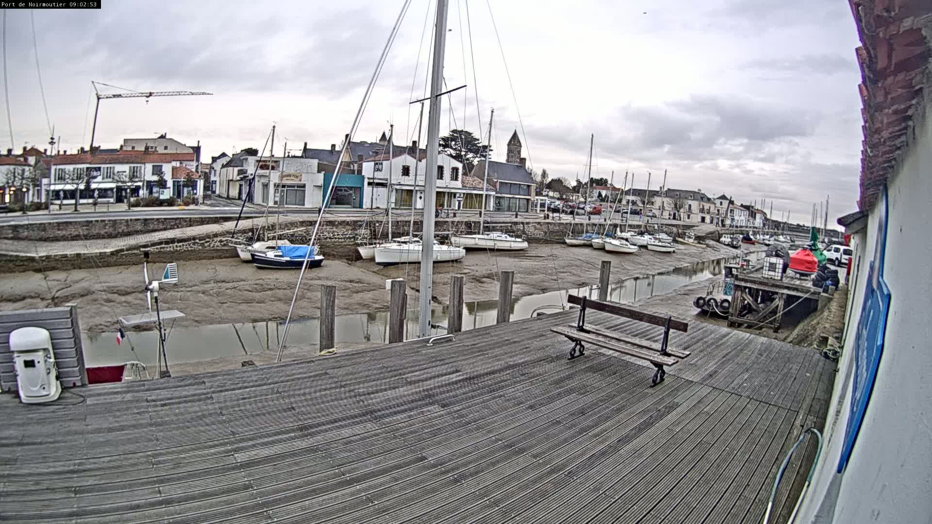 A wooden dock overlooks a harbor filled with sailboats at low tide under an overcast sky.