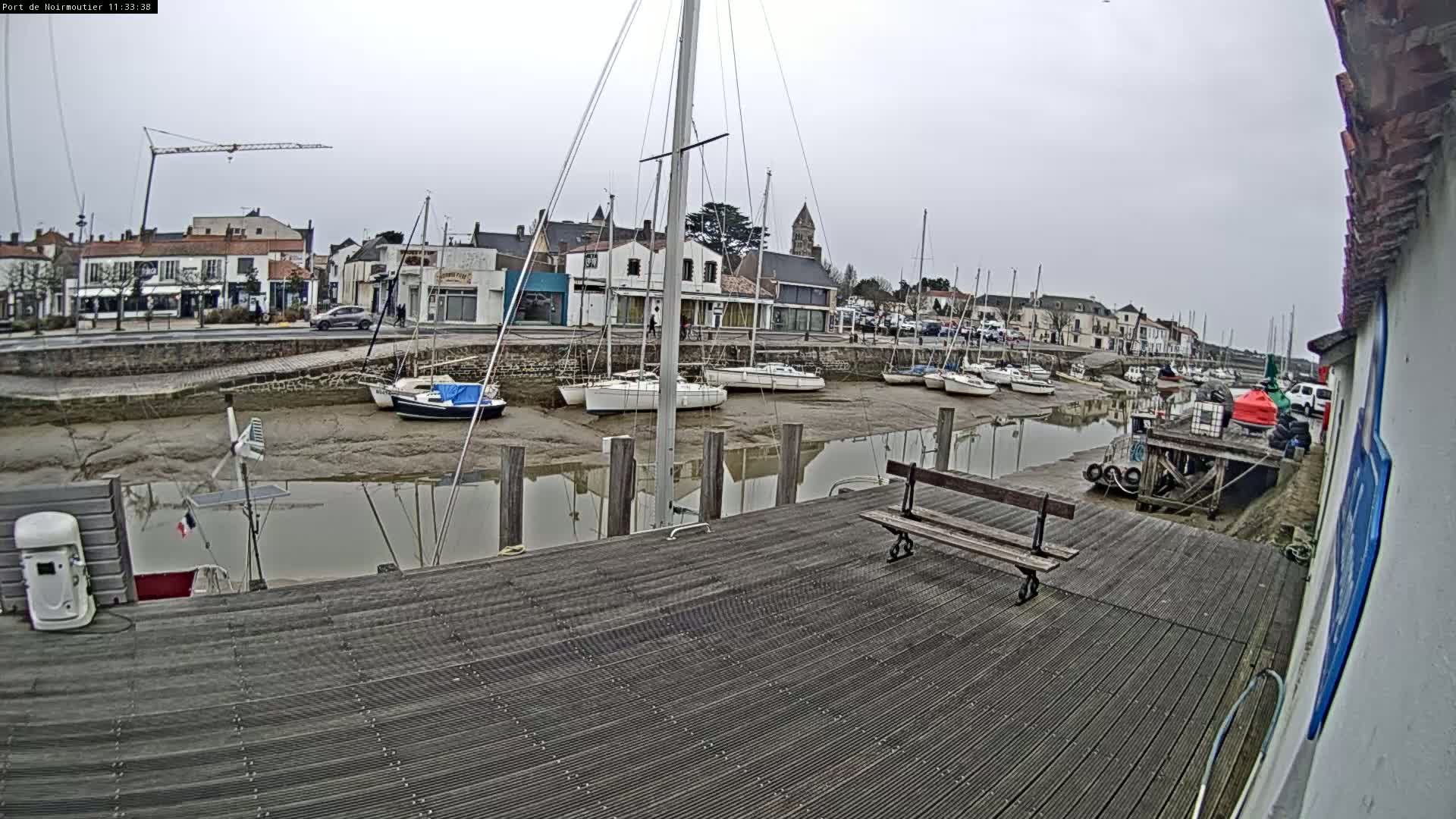 A wooden dock overlooks a calm harbor filled with sailboats at low tide on an overcast day.