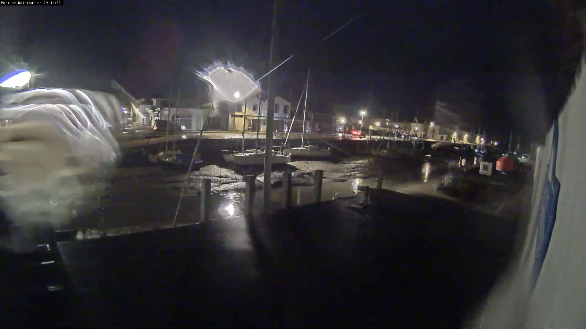 At night, a harbor with sailboats sits mostly dry at low tide under dim lighting.
