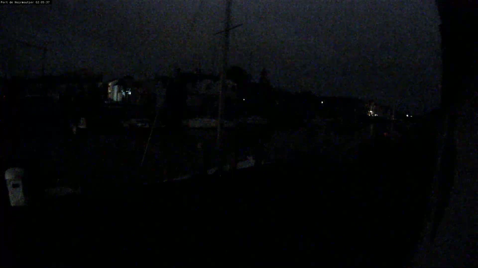 A dark nighttime harbor scene shows dimly lit buildings and a few boats.