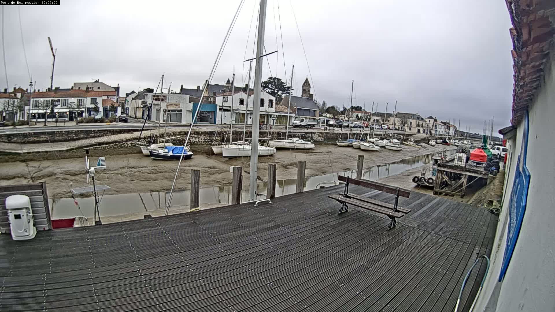 A dock with several sailboats moored in a harbor at low tide under an overcast sky.