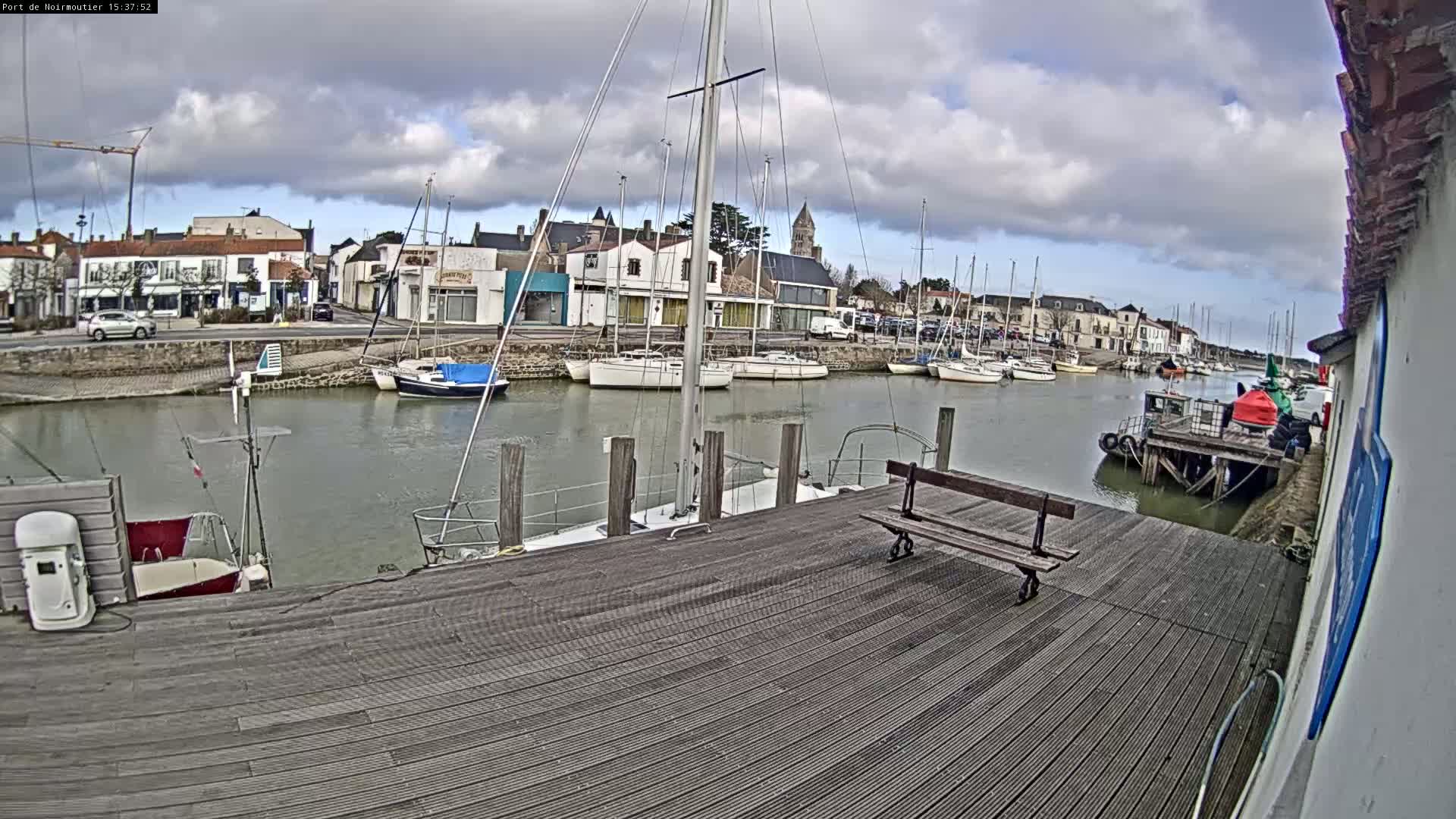 A wooden dock overlooks a calm harbor filled with sailboats under a partly cloudy sky.