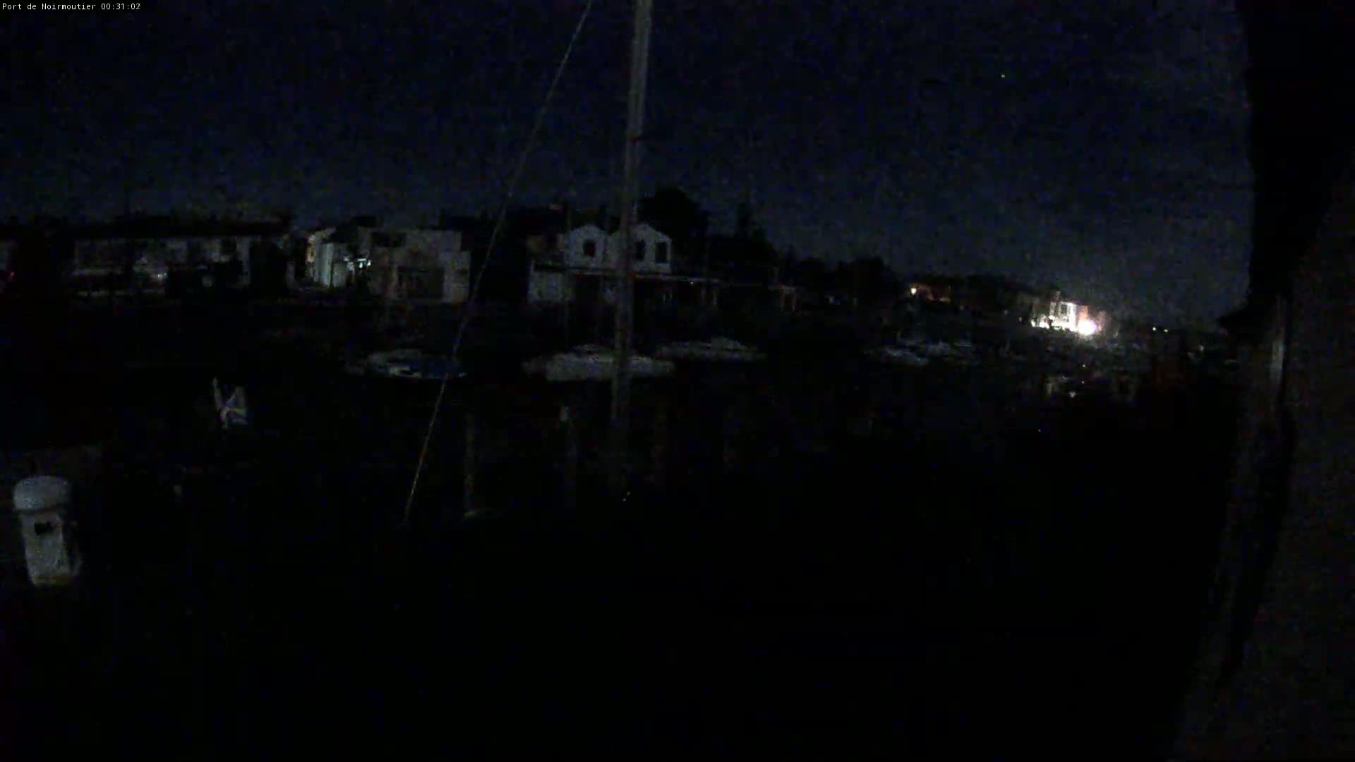 A dark, nighttime view of a harbor with boats and buildings under a mostly clear sky.