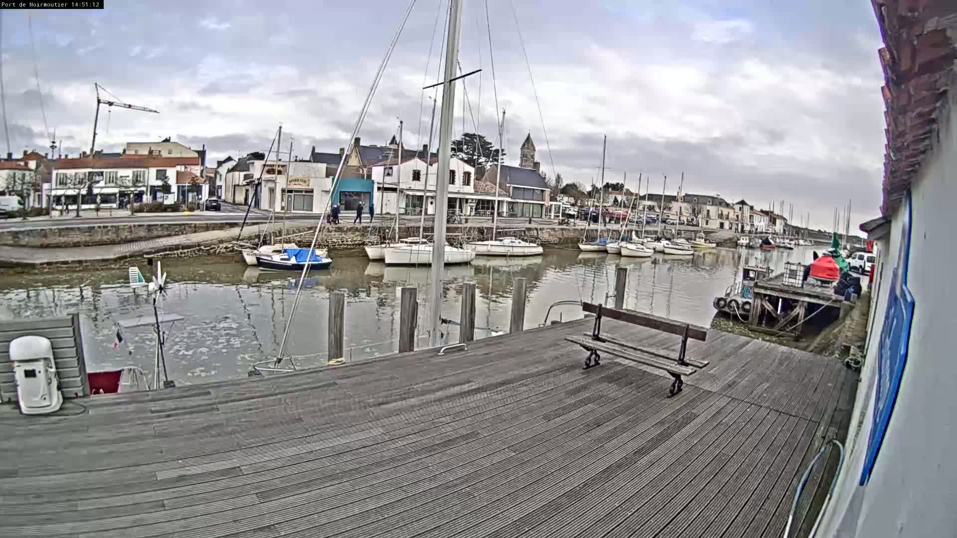 A wooden dock overlooks a calm harbor filled with sailboats, under a cloudy sky.