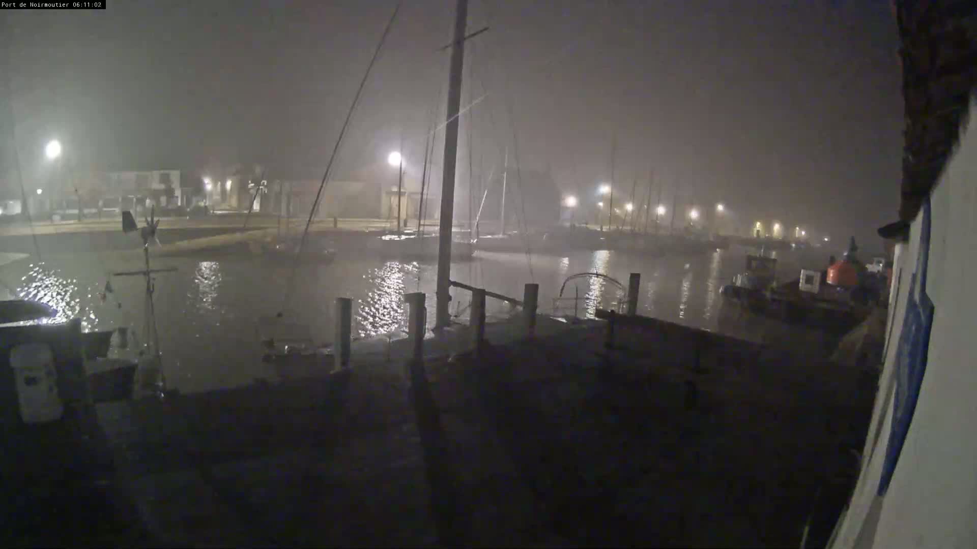 A nighttime view of a harbor filled with boats under foggy and stormy conditions.